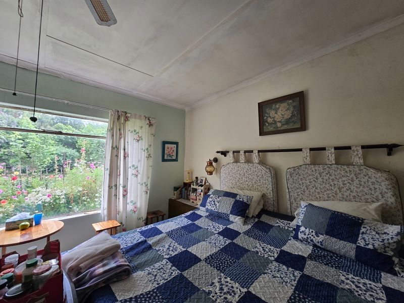 A bedroom featuring a large window with garden views and a ceiling fan. The room requires cosmetic updates to the ceiling and wall finishes.