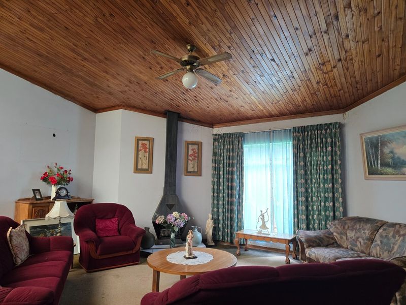 A living room featuring a distinctive wood-paneled ceiling, a central ceiling fan, and a freestanding fireplace, offering a cozy and traditional atmosphere.