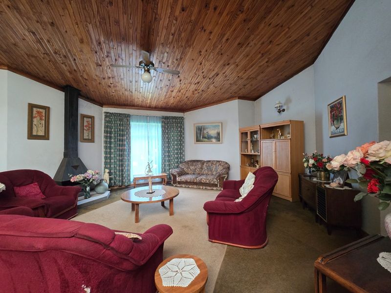 Spacious living room featuring a vaulted timber ceiling, a freestanding fireplace, and large windows, offering a comfortable and traditional living space.