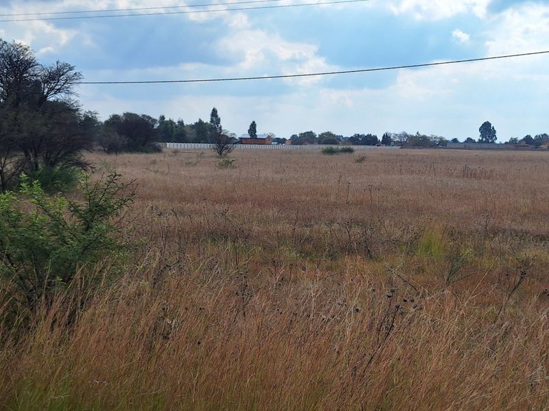 A wide, open vacant residential plot featuring natural grass cover and overhead power lines, suitable for future development.