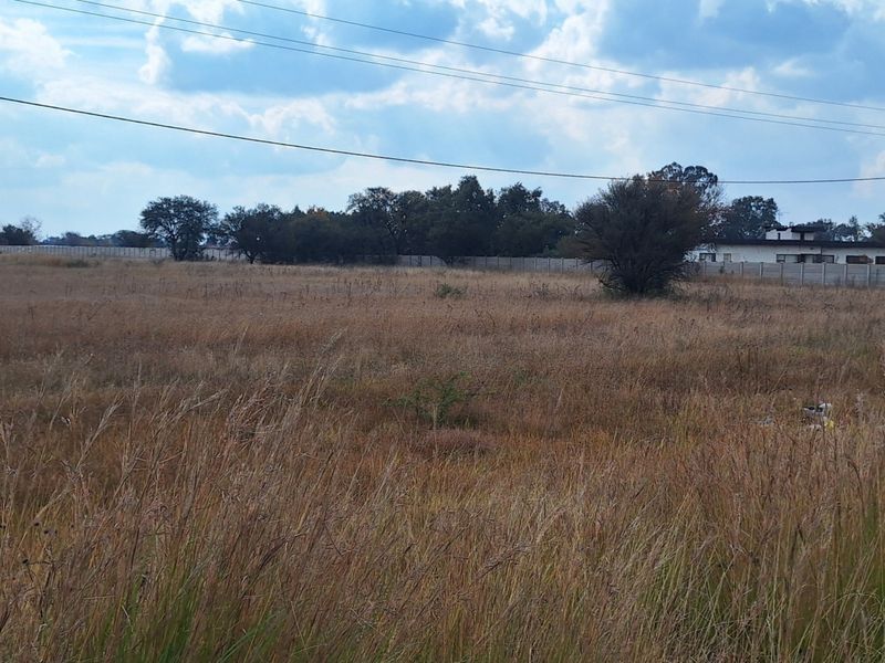 A wide-angle view of a vacant residential plot featuring dry grass, perimeter walling, and overhead power lines.