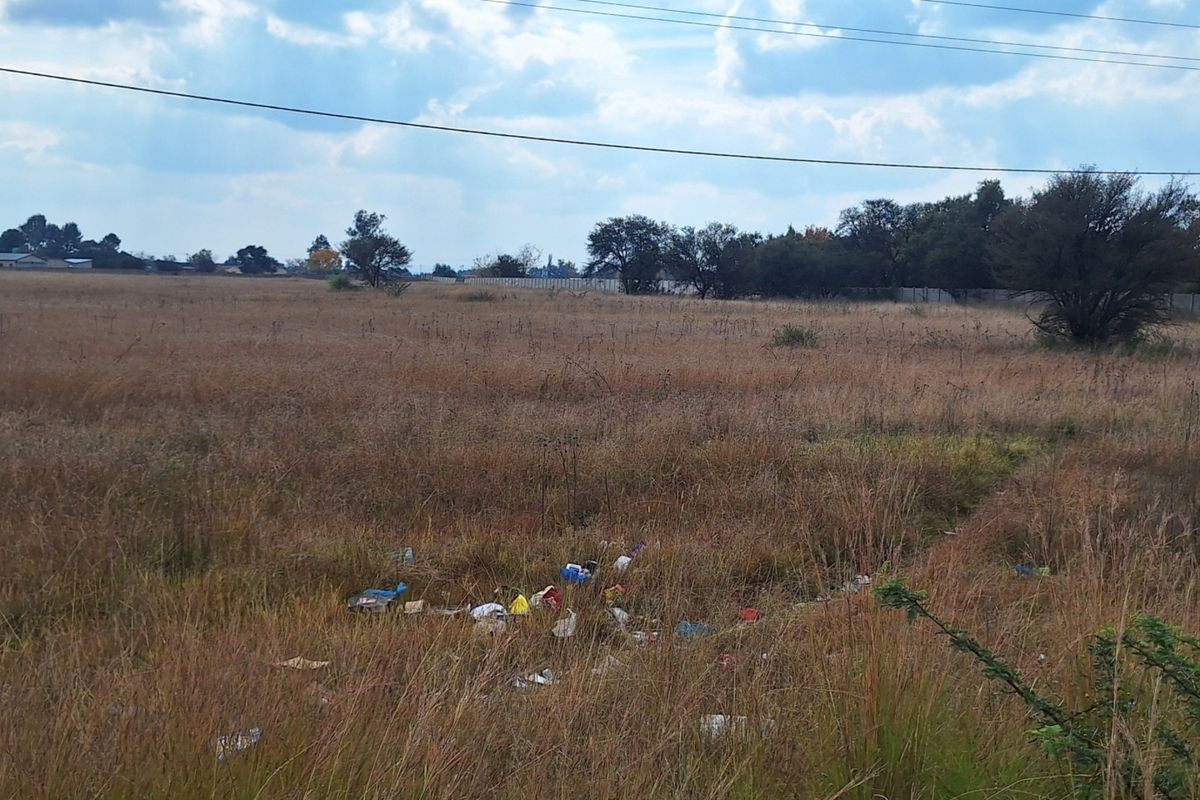 A view of a vacant residential plot featuring dry grass, scattered debris, and overhead power lines.