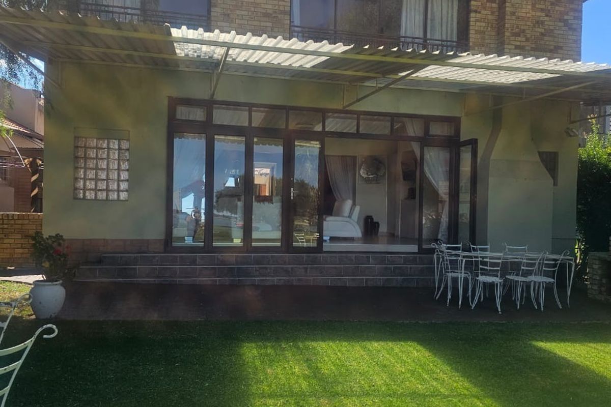 Rear view of a two-story brick house featuring a covered patio area, large glass sliding doors, and a well-maintained lawn.