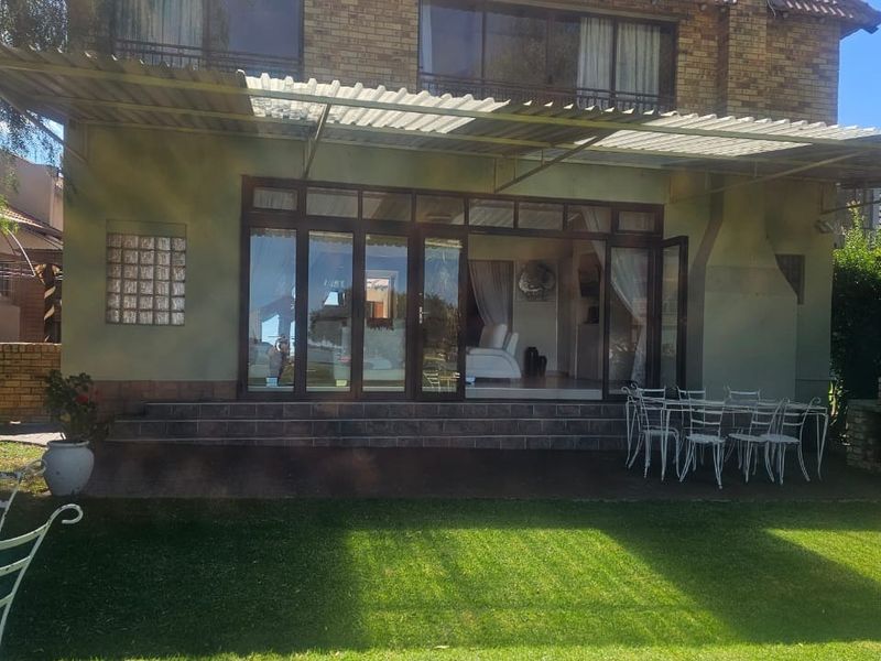 Rear view of a two-story brick house featuring a covered patio area, large glass sliding doors, and a well-maintained lawn.