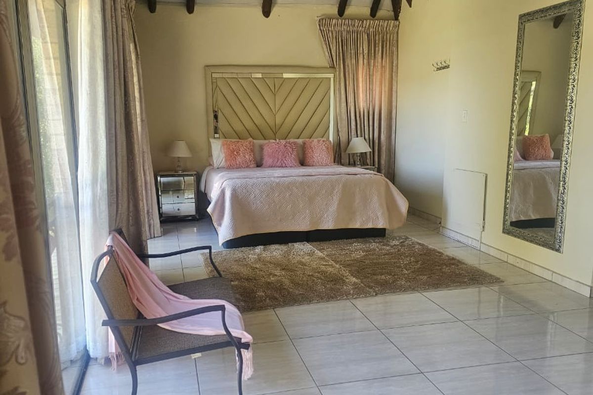 Spacious bedroom featuring a high vaulted ceiling with exposed timber beams, tiled flooring, and large sliding glass doors providing natural light.