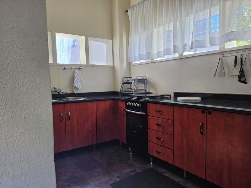 A functional kitchen featuring dark wood-look cabinetry, stone countertops, a freestanding oven, and tiled flooring, offering a practical layout for daily meal preparation.