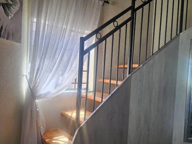 A staircase featuring wooden treads and a decorative metal balustrade, illuminated by natural light from a nearby window.