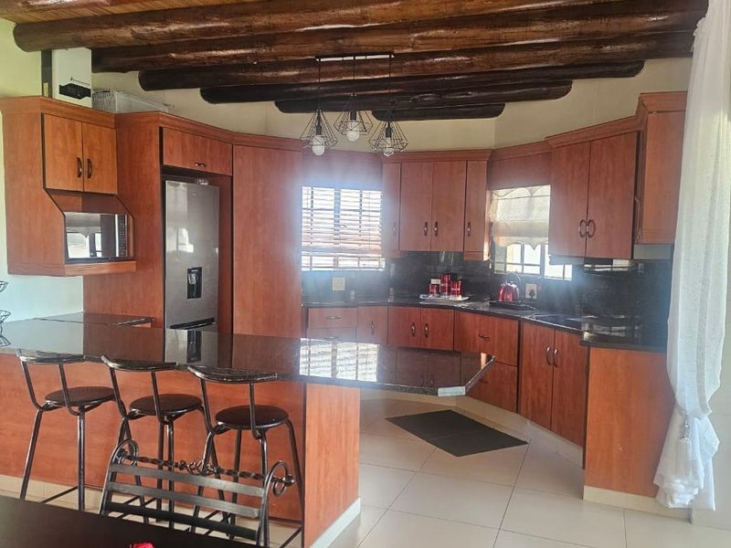 Spacious kitchen featuring warm timber ceiling beams, extensive wooden cabinetry, granite countertops, and a functional breakfast bar island.