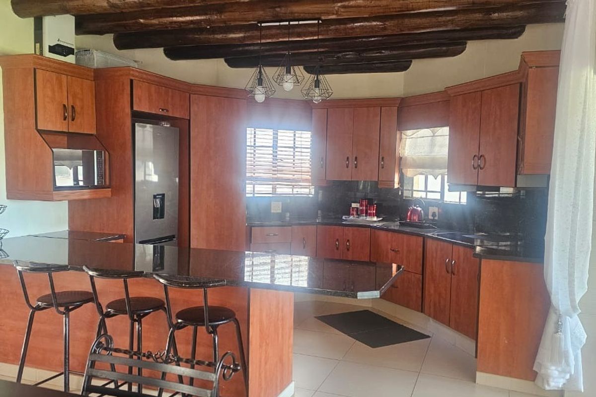 Spacious kitchen featuring warm timber ceiling beams, extensive wooden cabinetry, granite countertops, and a functional breakfast bar island.