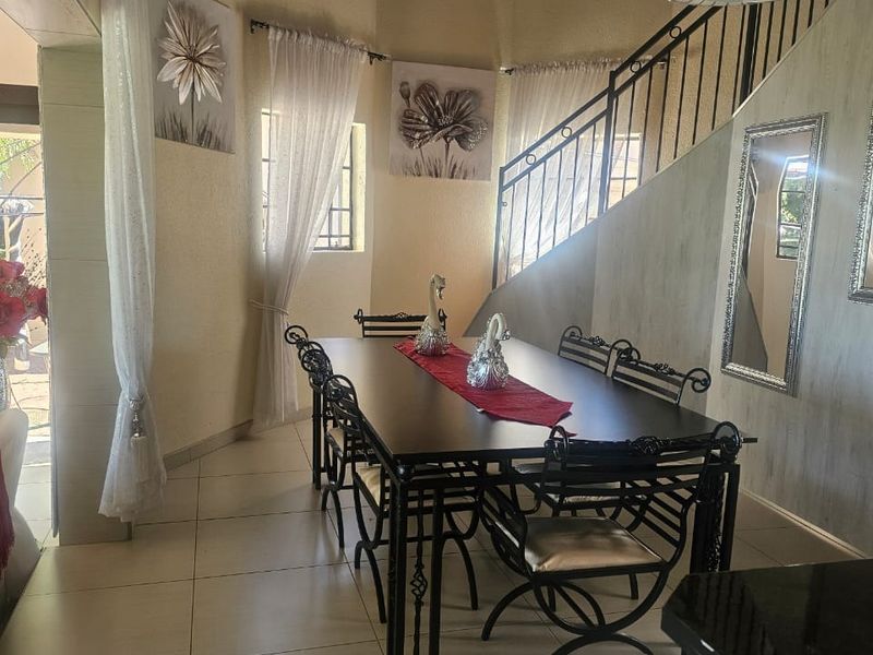 Dining area featuring tiled flooring, exposed timber ceiling beams, and a wrought iron staircase railing, creating a unique architectural space.