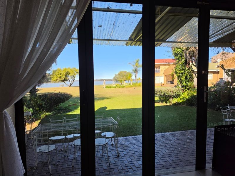 A covered patio area with brick paving and sliding glass doors, offering a view of the garden and waterfront.