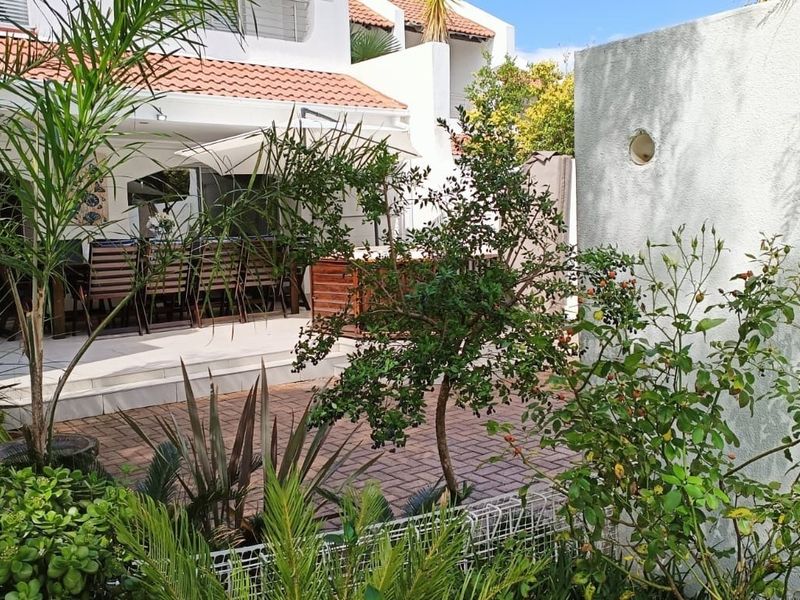 A private rear patio area featuring paved flooring, direct access to the townhouse via sliding doors, and established garden landscaping.