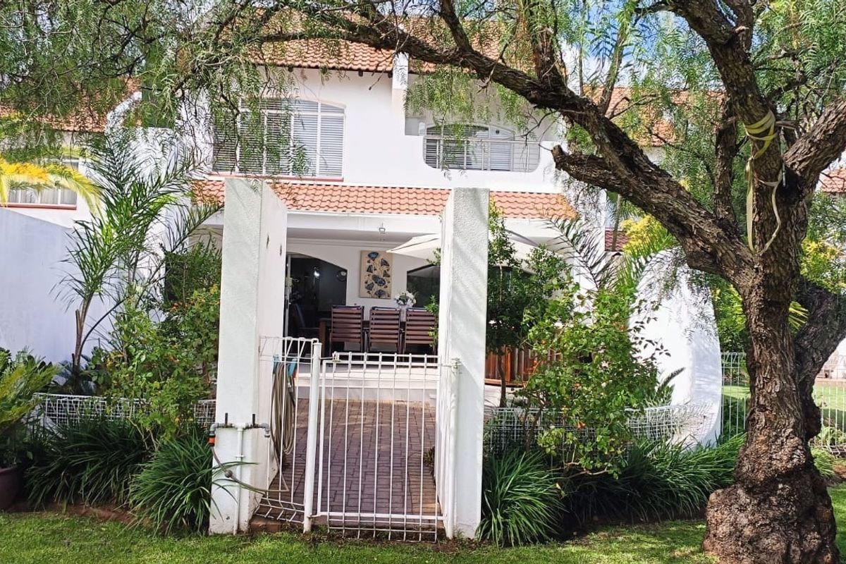 Rear view of a two-story townhouse featuring a paved entrance, covered patio, and balcony with terracotta roof tiles.