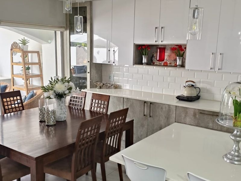 Modern open-plan kitchen and dining area featuring sleek white cabinetry, subway tile backsplash, and seamless access to the outdoor patio through sliding glass doors.
