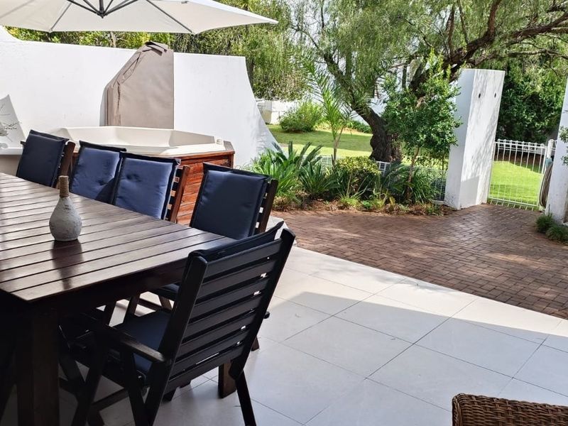 A well-maintained outdoor patio area featuring tiled flooring, leading out to a paved garden space with established greenery and secure boundary walls.