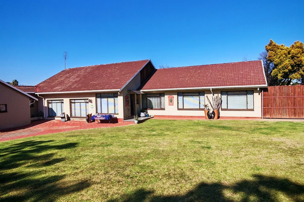 Rear view of a single-story house featuring a tiled roof, paved driveway, and a spacious lawn enclosed by timber fencing and boundary walls.