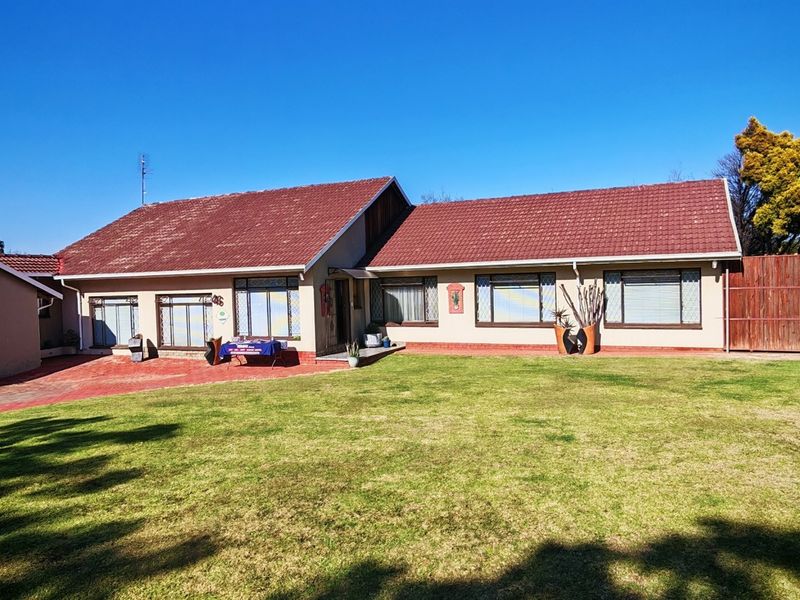 Rear view of a single-story house featuring a tiled roof, paved driveway, and a spacious lawn enclosed by timber fencing and boundary walls.