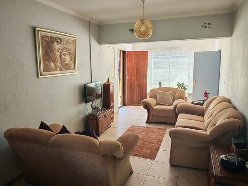 A functional living room featuring tiled flooring and natural light access through a secure entrance door.