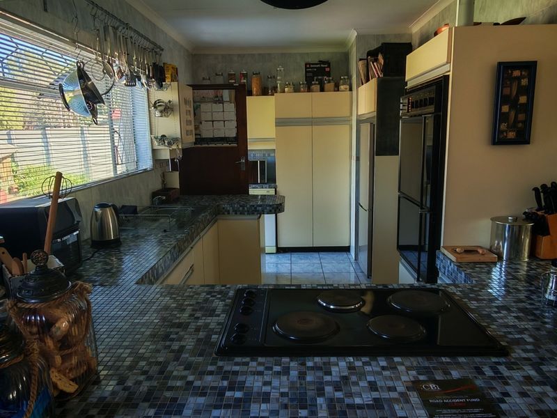 A functional kitchen featuring tiled countertops, built-in cabinetry, an integrated oven, and an electric hob, offering a practical layout with ample workspace.