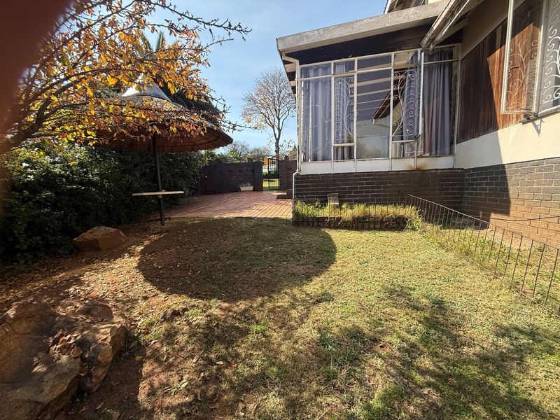 Rear garden area featuring a paved patio, enclosed sunroom, and established lawn, offering potential for outdoor landscaping and renovation.