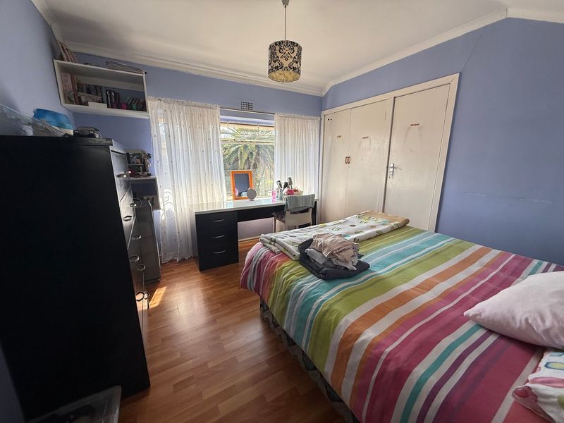 A functional bedroom featuring laminate flooring, built-in cupboards, and a built-in desk area, offering a practical layout with natural light.