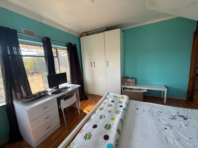 A bedroom featuring laminate flooring, a built-in wardrobe, and a window with security bars, finished with bright turquoise wall paint.