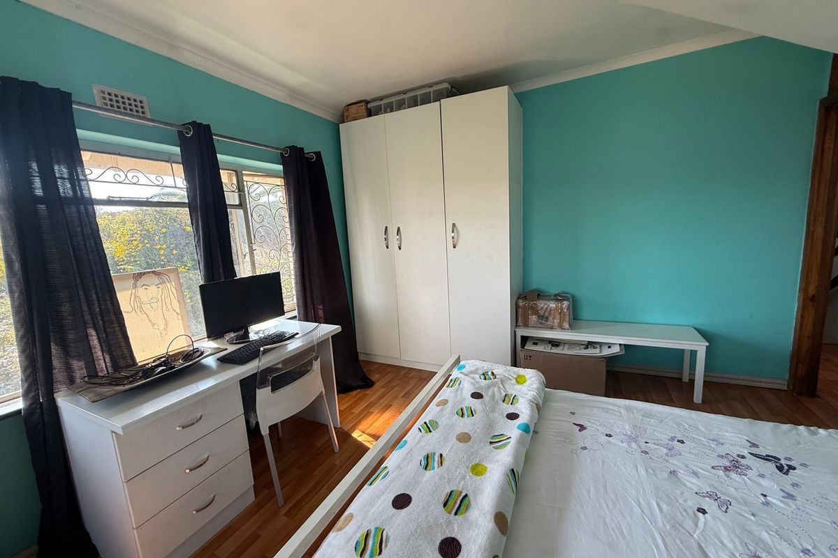 A bedroom featuring laminate flooring, a built-in wardrobe, and a window with security bars, finished with bright turquoise wall paint.