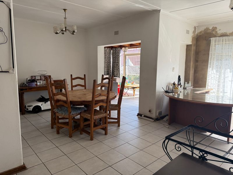 Open-plan dining and living area featuring tiled flooring and an unfinished wall section, offering potential for renovation and modern updates.