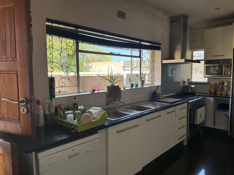 Functional kitchen featuring white cabinetry, stainless steel appliances, a gas stove with extractor, and a double sink with a view through security-barred windows.
