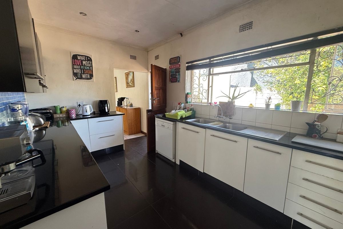 A functional kitchen featuring white cabinetry, black granite countertops, dark tiled flooring, and a large window with security bars.