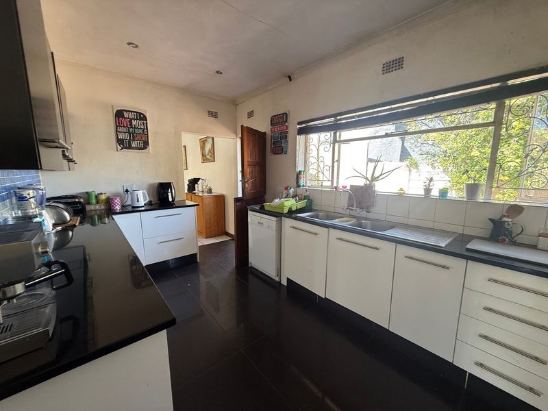 A functional kitchen featuring white cabinetry, black granite countertops, dark tiled flooring, and a large window with security bars.