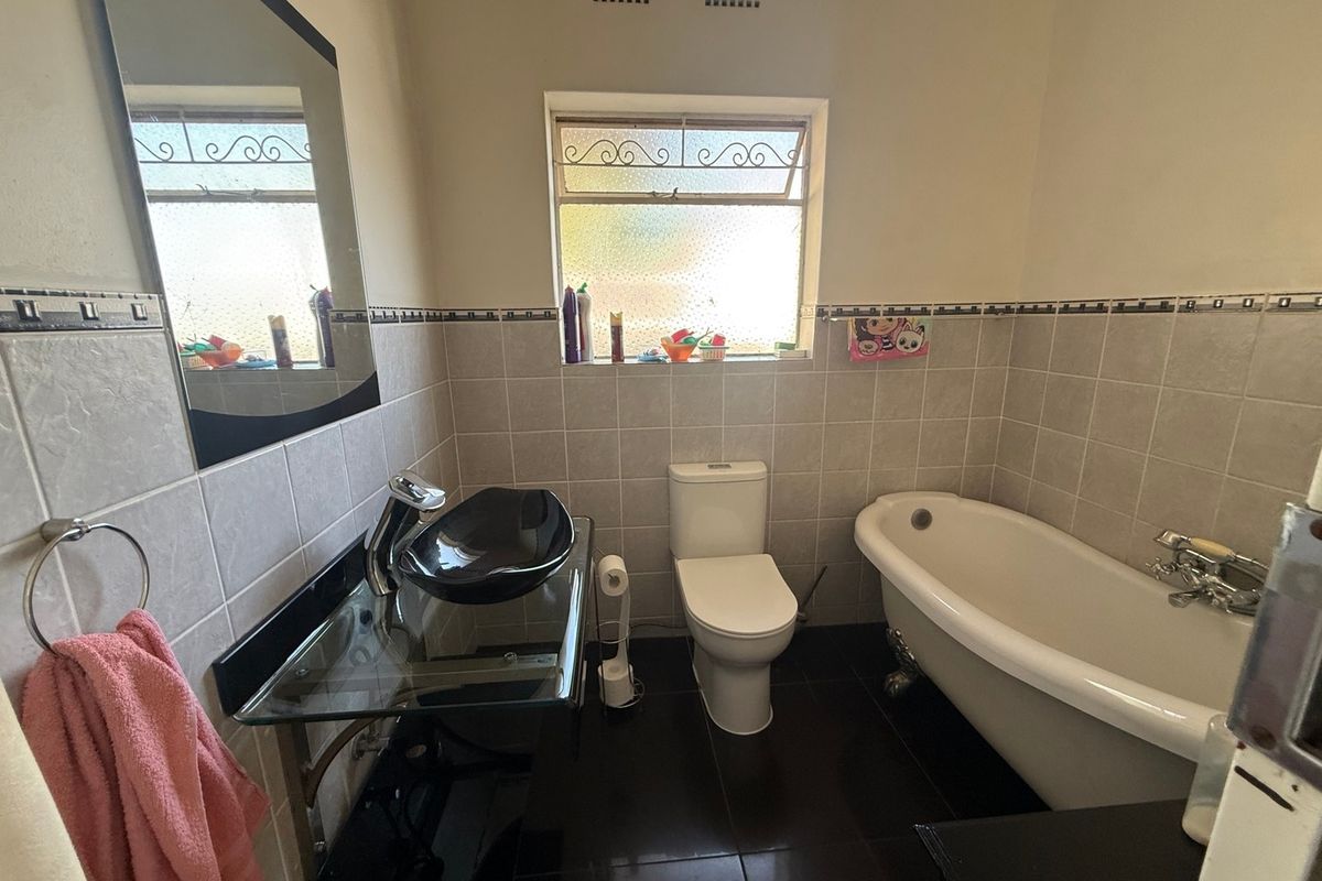 A bathroom featuring a clawfoot bathtub, a glass vanity with a black vessel sink, and tiled walls and flooring.