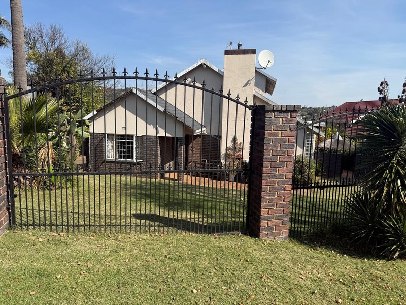 Front view of a residential house featuring a brick facade, tiled roof, chimney, and a secure wrought iron gate entrance.