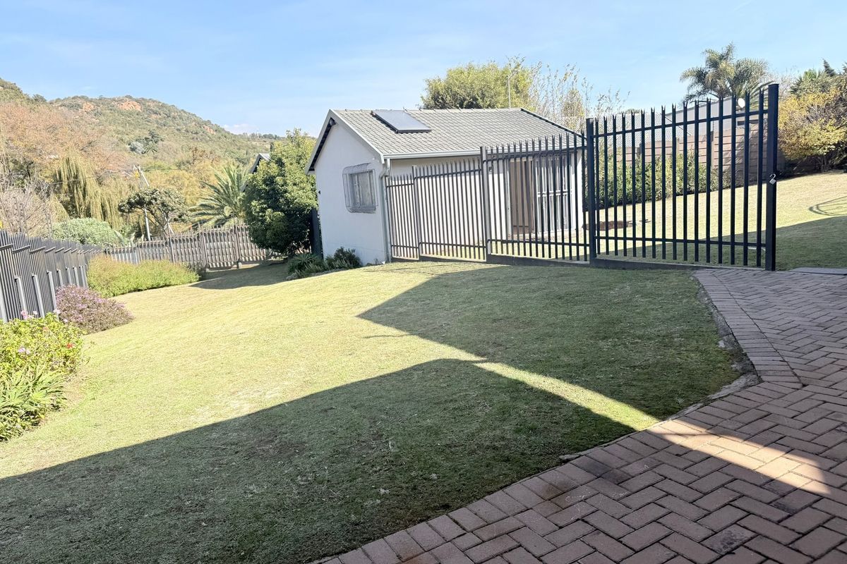 A view of the rear garden featuring a lawn, paved walkway, and a detached structure with a solar water heater and security fencing.