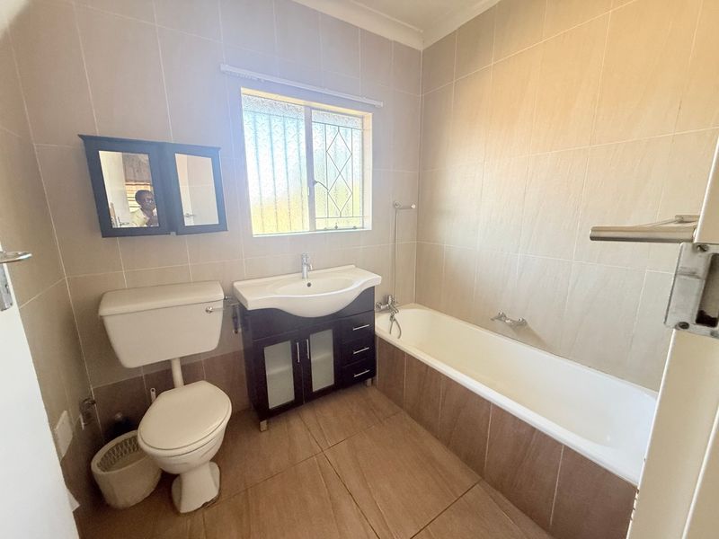 A functional bathroom featuring a built-in vanity, bathtub, and toilet with neutral wall and floor tiling.