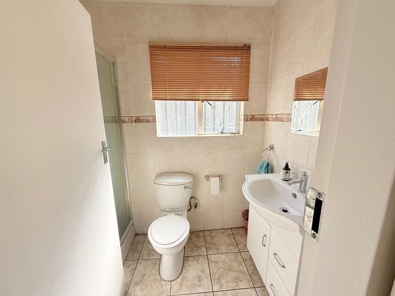 A functional bathroom featuring a vanity basin, toilet, and shower enclosure with neutral wall and floor tiling.
