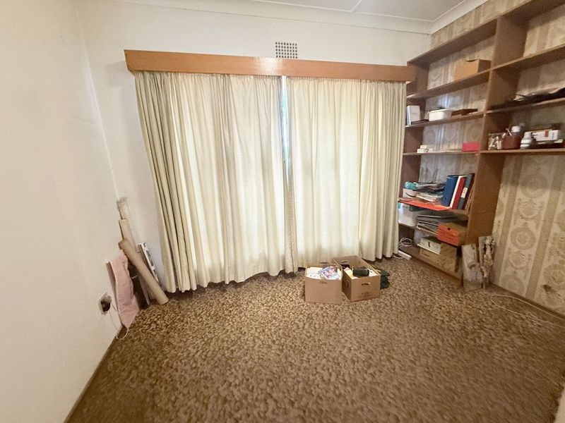 A bedroom featuring built-in shelving, dated wallpaper, and carpet flooring, offering potential for modernization and cosmetic updates.