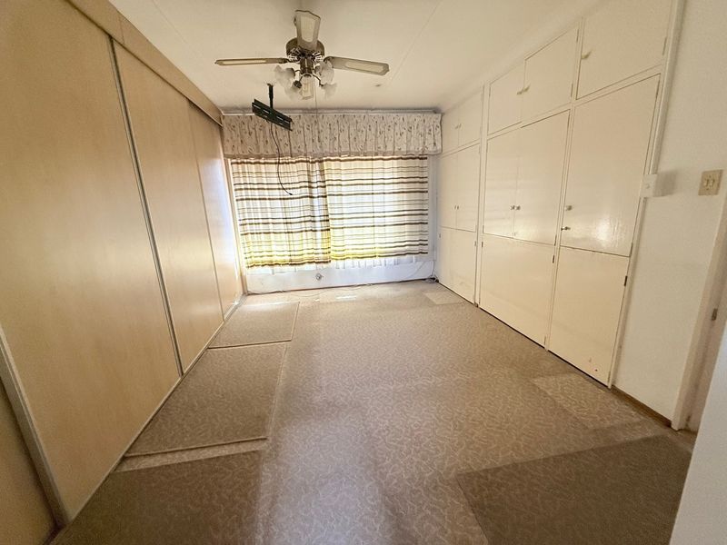 A spacious bedroom featuring extensive built-in storage, a ceiling fan, and neutral carpeting, offering a blank canvas for renovation or modernization.