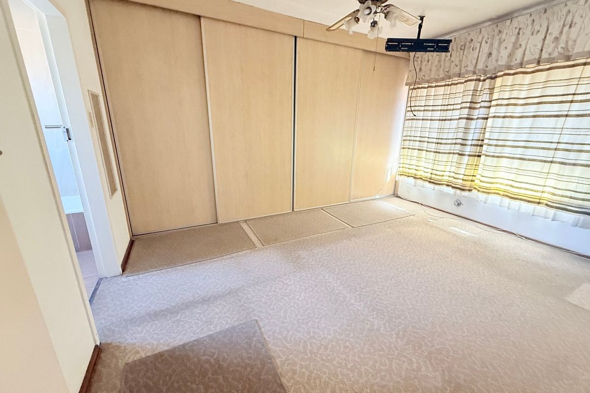 A spacious, empty bedroom featuring built-in cupboards, a ceiling fan, and carpeted flooring, offering a blank canvas for renovation.
