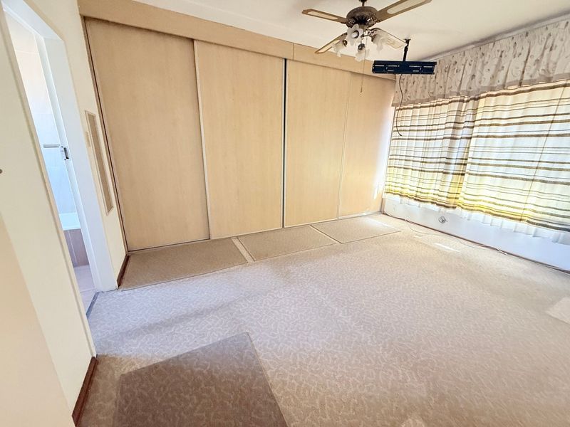 A spacious, empty bedroom featuring built-in cupboards, a ceiling fan, and carpeted flooring, offering a blank canvas for renovation.