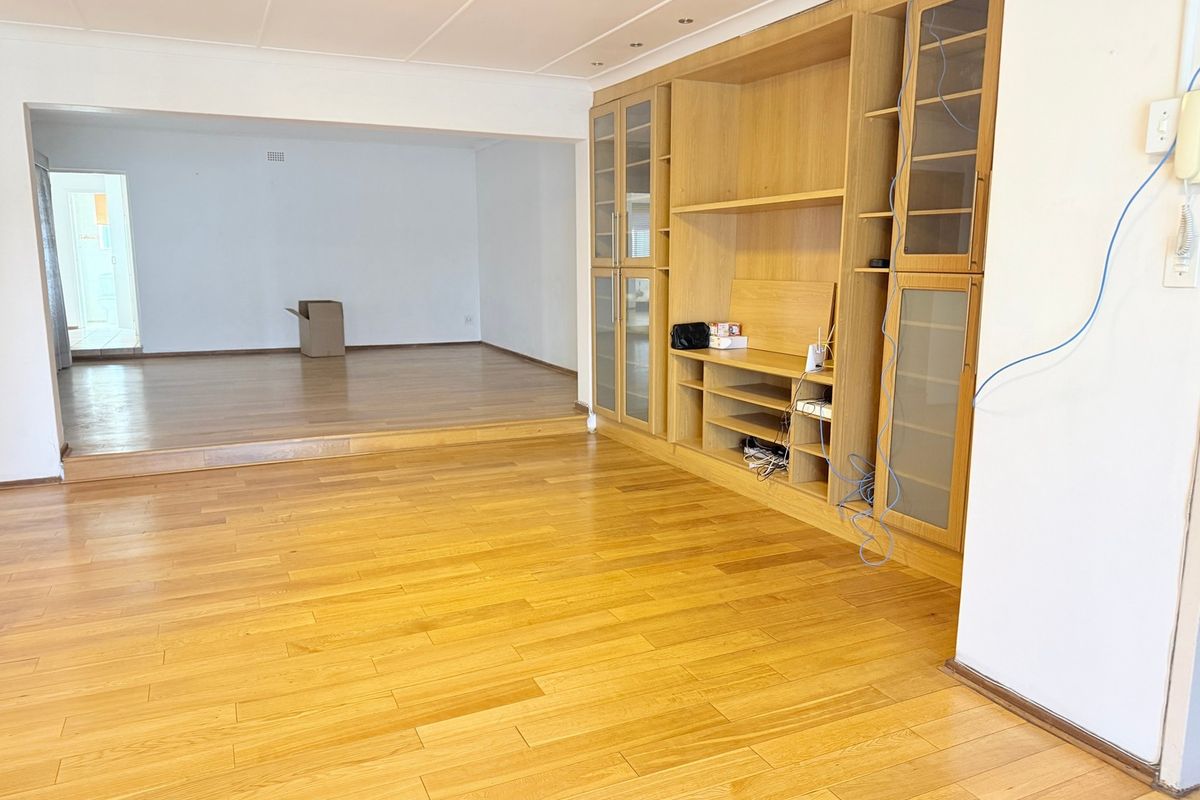 Spacious living area featuring polished hardwood flooring, a raised floor section, and extensive built-in wooden cabinetry with glass-fronted display units.