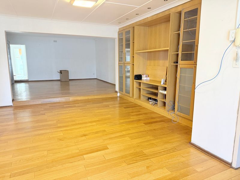 Spacious living area featuring polished hardwood flooring, a raised floor section, and extensive built-in wooden cabinetry with glass-fronted display units.