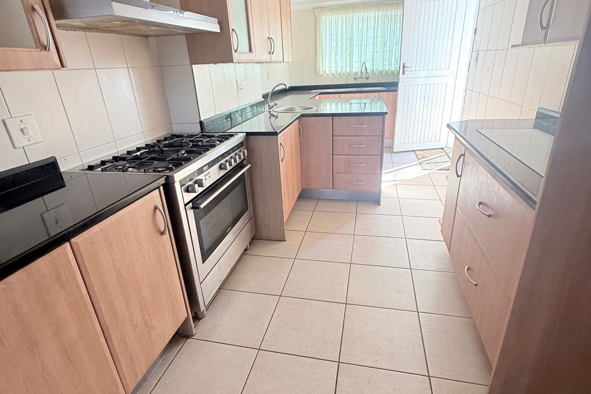 A functional kitchen featuring light wood cabinetry, granite countertops, a gas stove with extractor fan, and tiled flooring with direct access to the exterior.