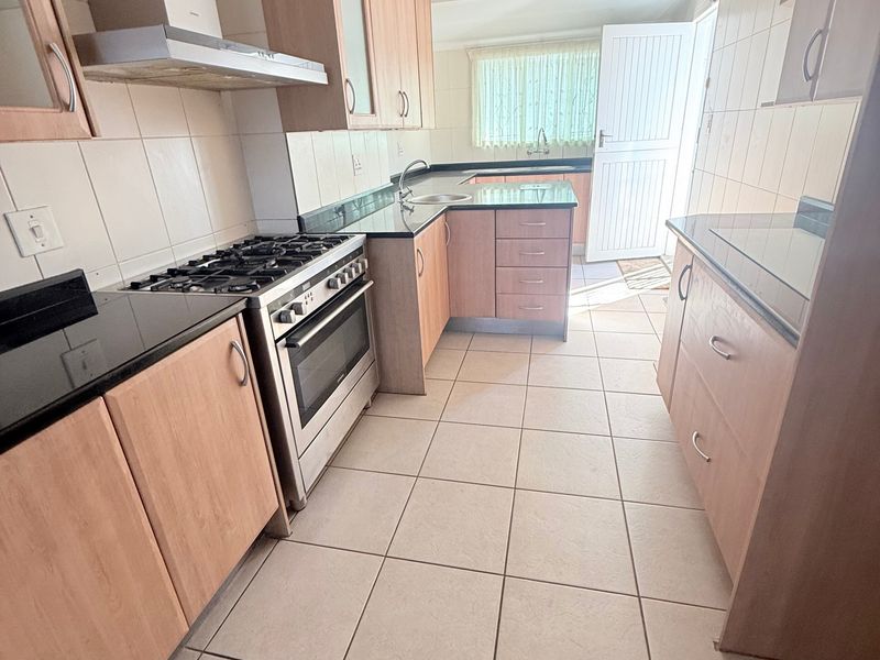 A functional kitchen featuring light wood cabinetry, granite countertops, a gas stove with extractor fan, and tiled flooring with direct access to the exterior.