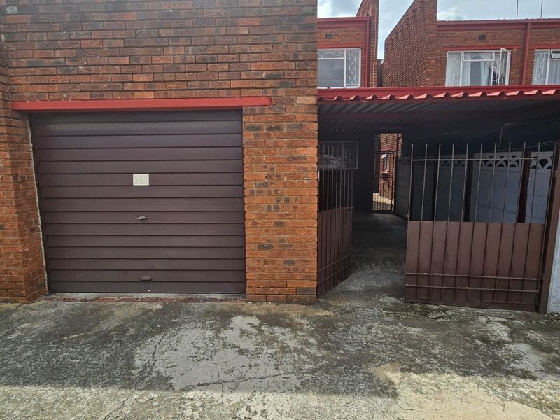 Front exterior view of a townhouse featuring a single garage, a covered carport area, and a metal security gate entrance.