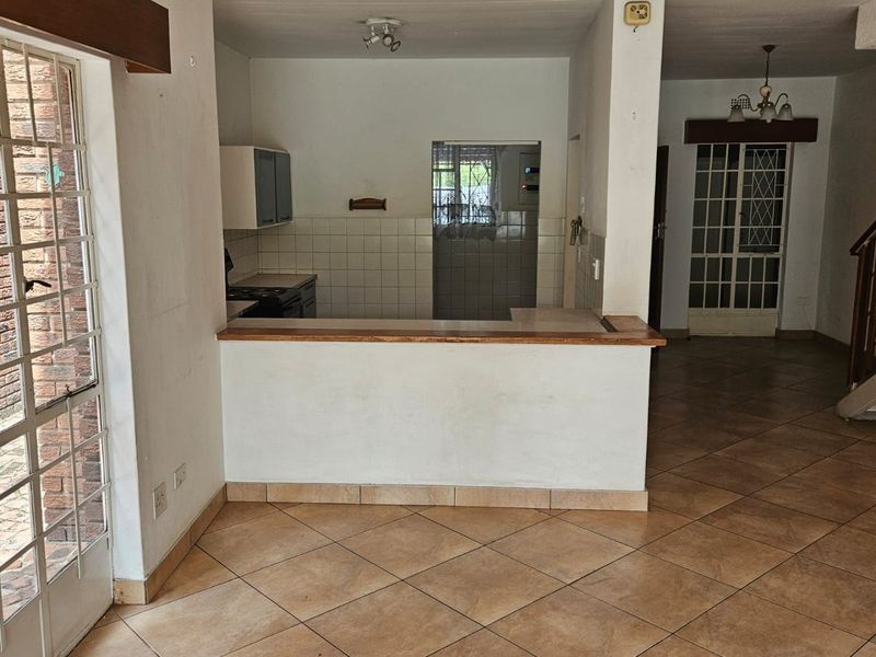 An open-plan living and kitchen area featuring tiled flooring, a breakfast bar, and direct access to an outdoor patio through a security gate.