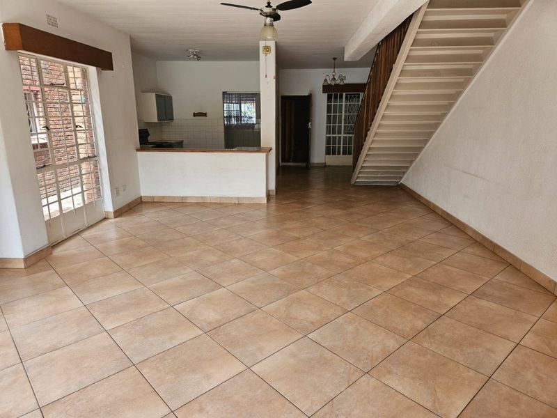 Spacious open-plan living area featuring tiled flooring, a central staircase, and a functional kitchen counter, offering a blank canvas for renovation.