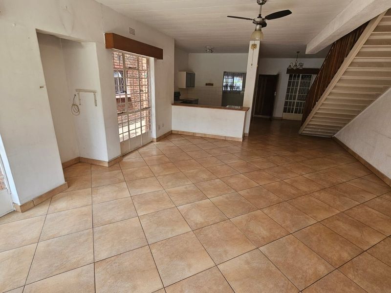 Spacious open-plan living area featuring tiled floors, a central staircase, and a breakfast counter connecting to the kitchen space.