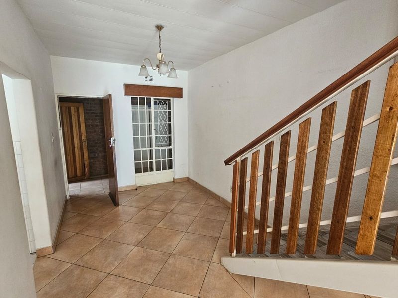An empty hallway featuring tiled flooring, a wooden staircase balustrade, and a security gate leading to an adjacent room.