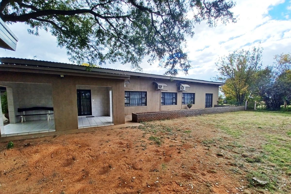 Rear view of the property featuring a covered patio, tiled flooring, security bars on windows, and a brick retaining wall set against a large garden.